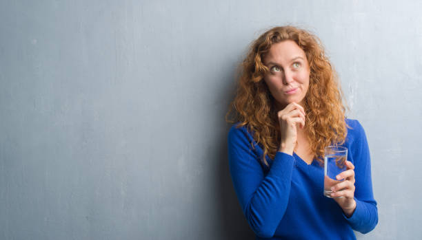 istock Young redhead woman over grey grunge wall drinking water serious face thinking about question, very confused idea 1043248286