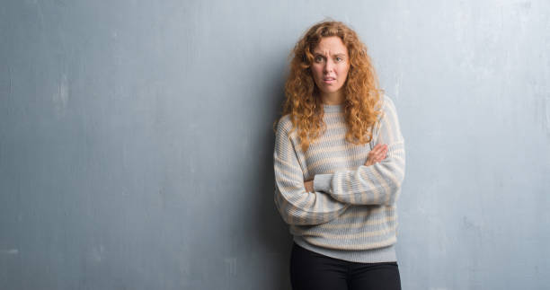 istock Young redhead woman over grey grunge wall skeptic and nervous, disapproving expression on face with crossed arms. Negative person. 1043255294