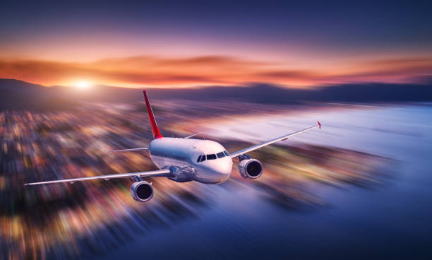 istock Airplane with motion blur effect is flying over sea coast at night. Landscape with passenger airplane, blurred buildings, city illumination, sea and sky. Aircraft. Business travel. Commercial plane 1043261612