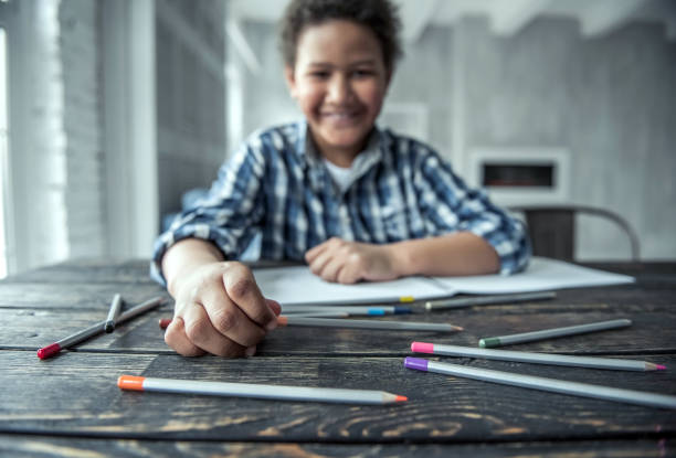 Afro American boy Afro American boy is drawing using colored pencils and smiling while sitting at the table at home, blurred, hand and some pencils in focus sad african child drawings stock pictures, royalty-free photos & images