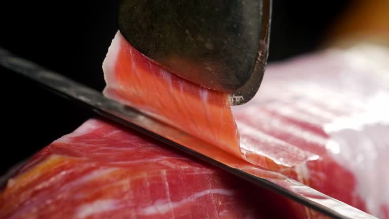 Close up macro of a chef who cuts a slice of ham, of excellent quality, with the knife according to tradition.