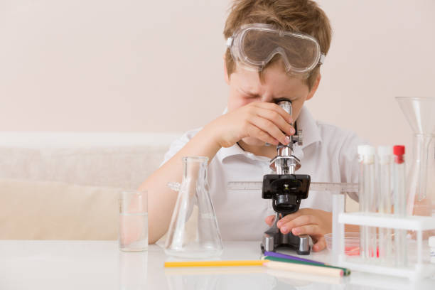 istock Cute elementary schoolboy looking into microscope at his desk at home. Young scientist making experiments in his home laboratory. Indoors. Child and science. Education concept. 1043281530