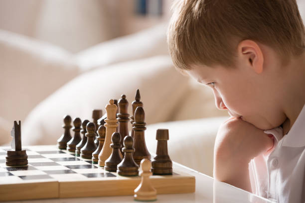 istock Boy playing chess in the room. Little clever boy concentrated and thinking while playing chess at home. 1043281744