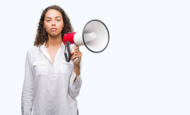 istock Young hispanic woman holding megaphone with a confident expression on smart face thinking serious 1043282718