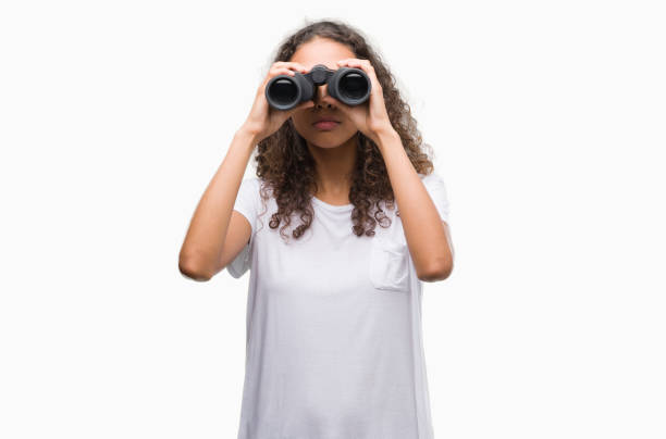 istock Young hispanic woman looking through binoculars with a confident expression on smart face thinking serious 1043288922