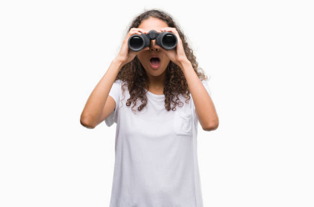 istock Young hispanic woman looking through binoculars scared in shock with a surprise face, afraid and excited with fear expression 1043288948