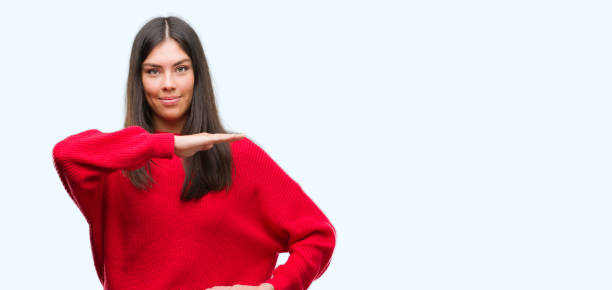 istock Young beautiful hispanic wearing red sweater gesturing with hands showing big and large size sign, measure symbol. Smiling looking at the camera. Measuring concept. 1043291788