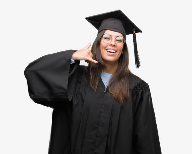istock Young hispanic woman wearing graduated cap and uniform smiling doing phone gesture with hand and fingers like talking on the telephone. Communicating concepts. 1043292522