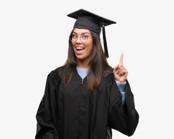 istock Young hispanic woman wearing graduated cap and uniform pointing finger up with successful idea. Exited and happy. Number one. 1043292690