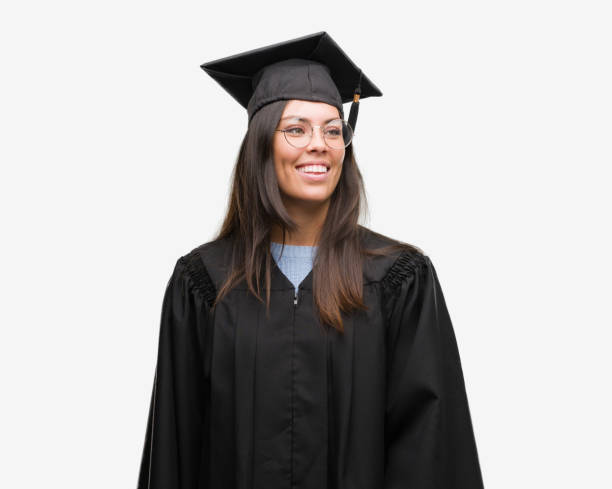 young hispanic woman wearing graduated cap and uniform looking away to side with smile on face, natural expression. laughing confident. - graduation student women beauty imagens e fotografias de stock