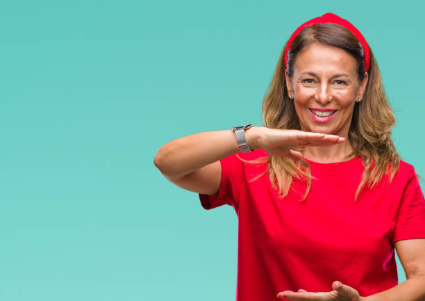 istock Middle age senior hispanic woman over isolated background gesturing with hands showing big and large size sign, measure symbol. Smiling looking at the camera. Measuring concept. 1043295490