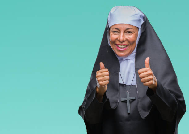 istock Middle age senior christian catholic nun woman over isolated background approving doing positive gesture with hand, thumbs up smiling and happy for success. Looking at the camera, winner gesture. 1043295566