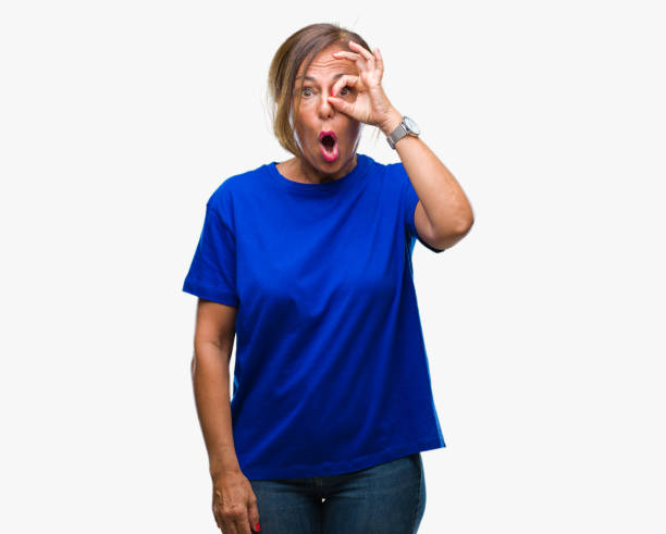 istock Middle age senior hispanic woman over isolated background doing ok gesture shocked with surprised face, eye looking through fingers. Unbelieving expression. 1043295848
