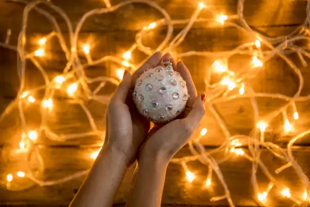 Woman's hand holding a christmas ornament shot on top of wooden background with Christmas lights