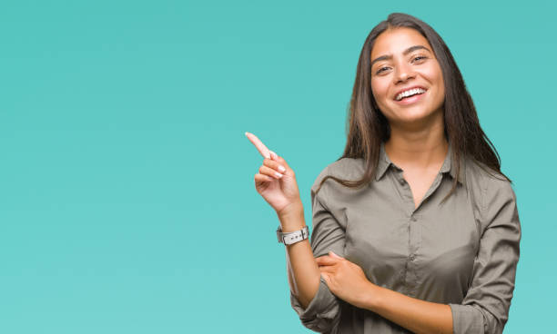 joven árabe mujer hermosa sobre fondo aislado con una gran sonrisa en la cara, señalando con la mano y del dedo al lado mirando a la cámara. - one finger fotografías e imágenes de stock