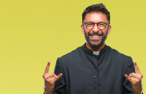 istock Adult hispanic catholic priest man over isolated background shouting with crazy expression doing rock symbol with hands up. Music star. Heavy concept. 1043320184