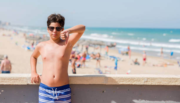 niño de vacaciones en la playa con cara enfadada, signo negativo que muestra aversión con los pulgares hacia abajo, concepto de rechazo - furious blue little boys caucasian fotografías e imágenes de stock