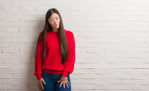 istock Young Chinese woman over brick wall making fish face with lips, crazy and comical gesture. Funny expression. 1043335336