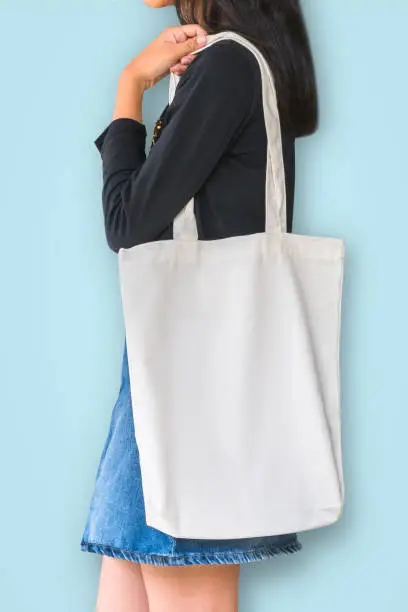 White tote bag mockup template cotton canvas fabric texture on girl shoulder (isolated with clipping path) on blue background