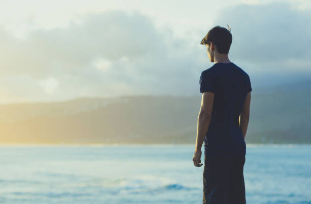 jeune homme méditant sur la falaise supérieure océan pendant le coucher du soleil. - sea zen like landscape water photos et images de collection