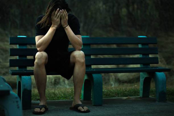 istock Depressed man sitting on a park bench covering his face with his hands 1043341432