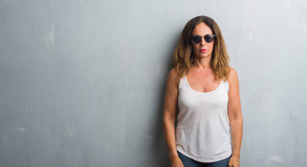 istock Middle age hispanic woman over grey wall wearing sunglasses with serious expression on face. Simple and natural looking at the camera. 1043350366
