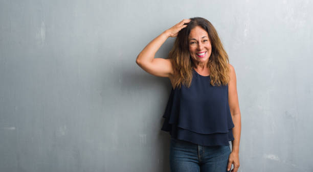 istock Middle age hispanic woman standing over grey grunge wall confuse and wonder about question. Uncertain with doubt, thinking with hand on head. Pensive concept. 1043352908