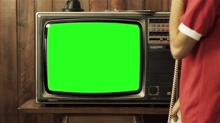 Teenage Boy Talking On Old Phone Near Television With Green Screen.