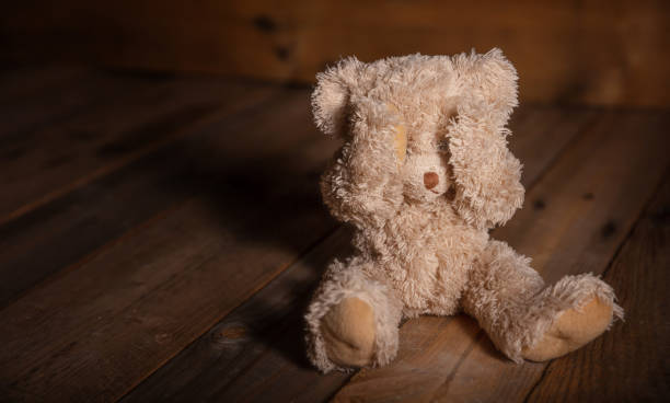 istock Child abuse.Teddy bear covering eyes, dark empty background, copy space 1043431674