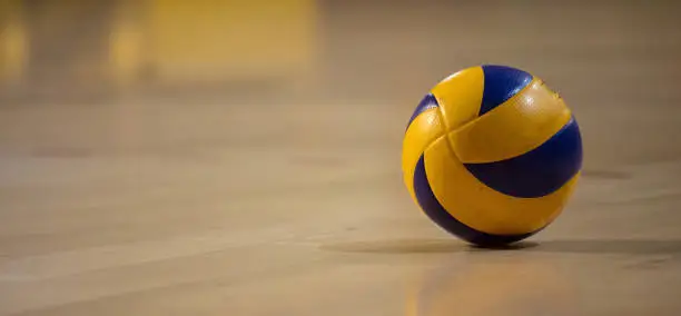 Volleyball ball, blue-yellow, with reflection. Blurred wooden parquetry background. Banner, space for text, close up view with details.