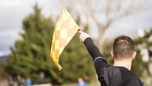 Photo of Soccer referee assistant raises the flag with his hand. Blur blue sky, nature, players background, close up view, details.