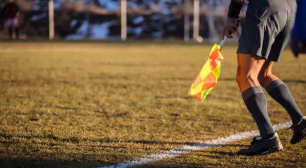 Football soccer arbiter assistant moves at sideline observing the match with flag at hands. Blurred green field and nature background, close up view, banner, space.
