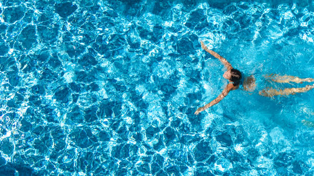 Aerial drone view of active girl in swimming pool from above, yong woman swims in blue water, tropical vacation, holiday on resort concept Aerial drone view of active girl in swimming pool from above, yong woman swims in blue water, tropical vacation, holiday on resort concept swimming pool stock pictures, royalty-free photos & images