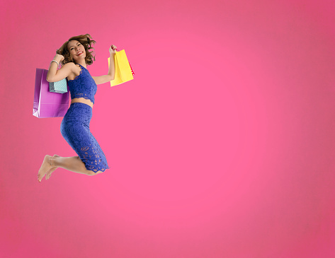 Happy Asian woman jumping and holding fancy shopping bags on a pink background copy space