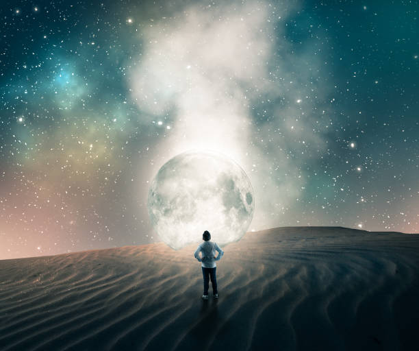 istock Young man in front of a moon fallen in the desert. 1043441532