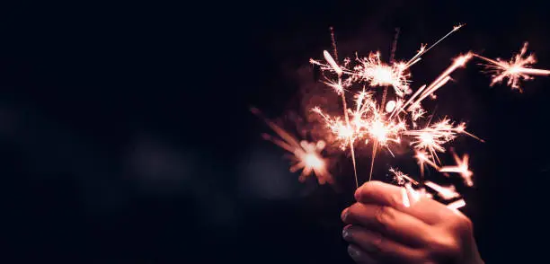 Photo of Hand holding burning Sparkler blast on a black bokeh background at night,holiday celebration event party,dark vintage tone