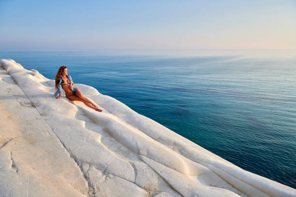 夕暮れ時、岩から海の景色を楽しんでいる若い女性 ストックフォト