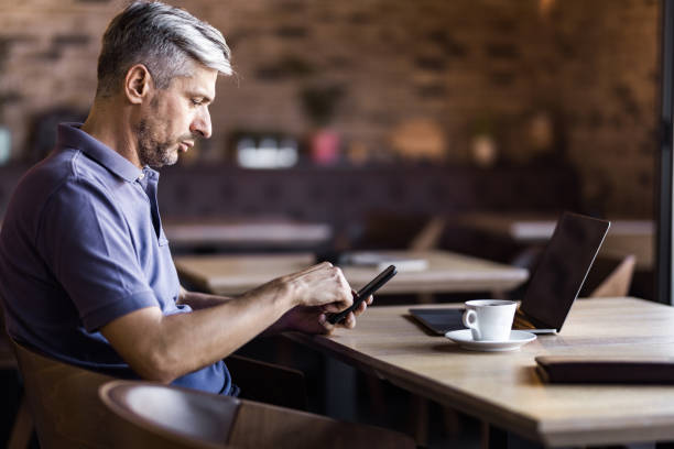 istock Profile view of mid adult man using mobile phone in a cafe. 1043471130