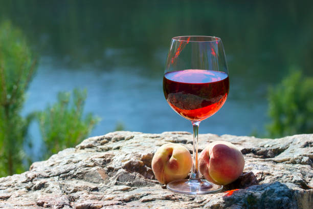 ワイン グラス赤ワインと桃が川の上の岩の上 - scotch on the rock ストックフォトと画像