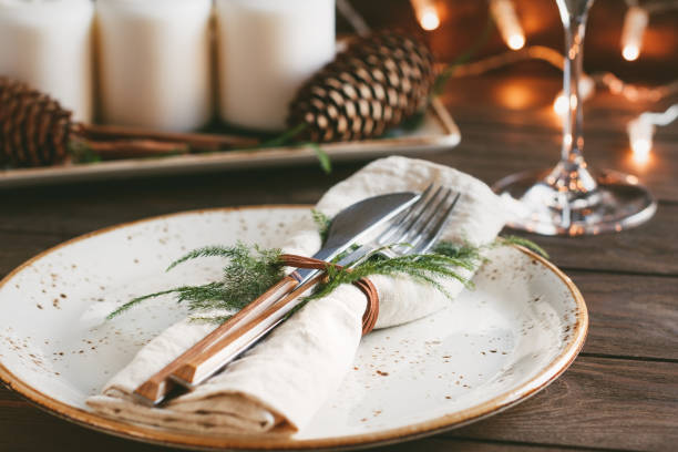 istock Thanksgiving table setting among white candles and cones. Ceramic plate with fork and knife on a linen napkin. The concept of a festive dinner. 1043479784