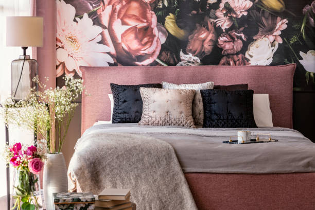 Pink and grey bed with cushions in patterned bedroom interior with flowers and lamp. Real photo Pink and grey bed with cushions in patterned bedroom interior with flowers and lamp. Real photo bedroom wallpaper stock pictures, royalty-free photos & images