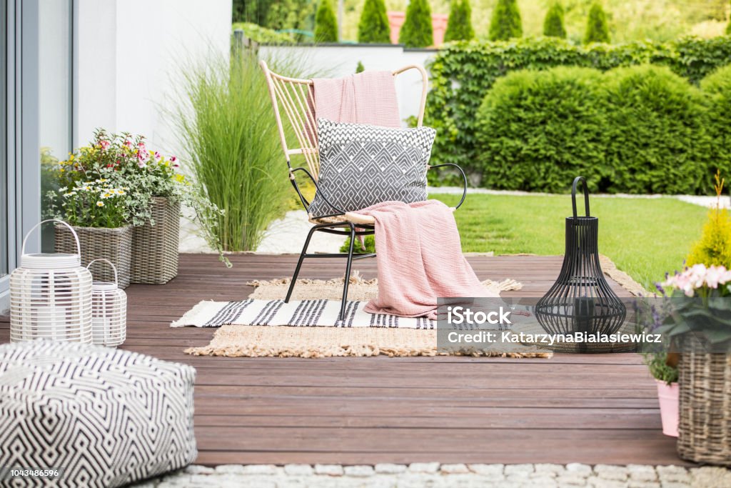 Real photo of a white pillow and pink blanket on a rattan chair standing in the garden of a luxurious house Yard - Grounds Stock Photo