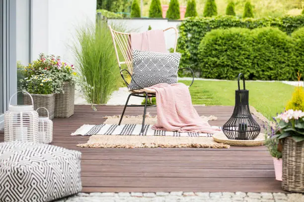 Photo of Real photo of a white pillow and pink blanket on a rattan chair standing in the garden of a luxurious house