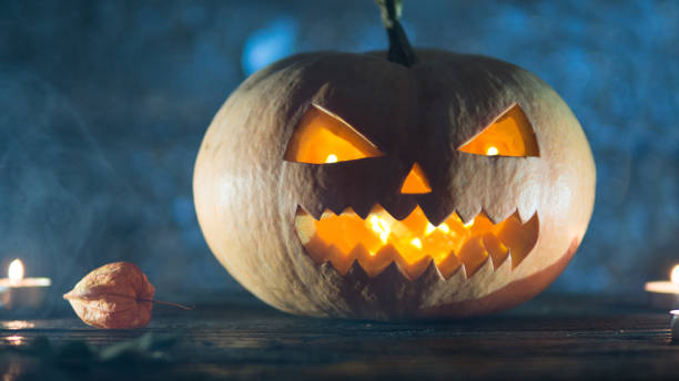 istock Cool pumpkin killer on Halloween in smoke on dark background with candles 1043487692