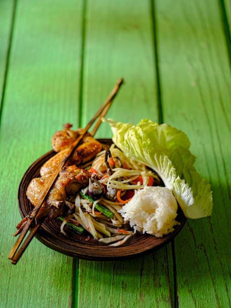 Fresh Som Tam Boo, a popular and favorite Thai food dish made of young papaya, chili, tomatoes, palm sugar and freshwater crab, served with grilled chicken wings and stick rice. Set on a lacquered plate on an old green wooden table. This dish is popular in the North and North Eastern part of Thailand and is normally eaten with ones fingers. Shallow depth of field. som tam boo, un plato popular y favorito de comida tailandesa de jóvenes rebanada de papaya, ají, tomate, azúcar de palma y cangrejo de agua dulce, servido con alitas de pollo a la brasa y arroz pegajoso en una vieja mesa de madera verde.