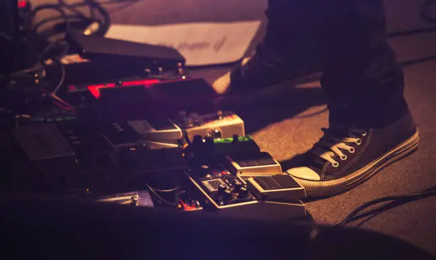 Electric guitar players legs on a stage with set of distortion effect pedals, rock music background