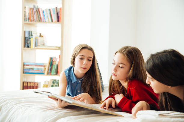 istock Three Happy Sisters Lying in Bedroom and Reading a Book. 1043515268