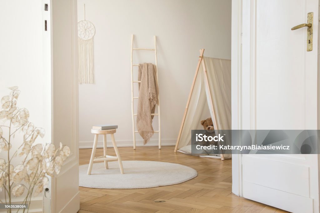 Real photo through the door of kid room interior with blanket on ladder, stool with book, play tent with teddy bear and herringbone parquet Herringbone Stock Photo