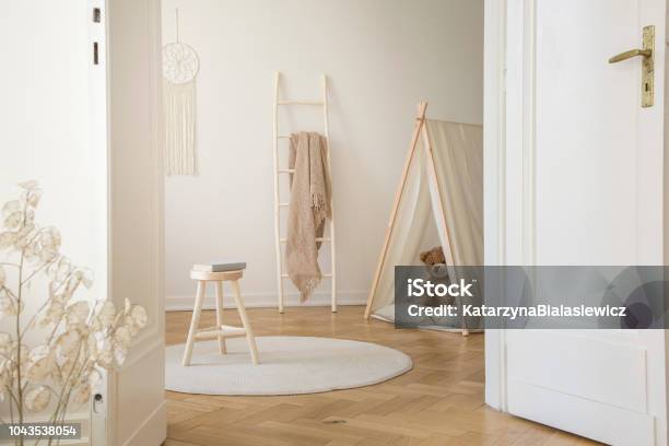Real Photo Through The Door Of Kid Room Interior With Blanket On Ladder Stool With Book Play Tent With Teddy Bear And Herringbone Parquet Stock Photo - Download Image Now