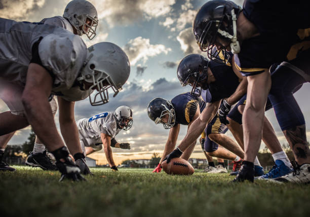 Below view of American football players on a beginning of the match. Low angle view of American football players confronting before the beginning of a match. offensive line stock pictures, royalty-free photos & images